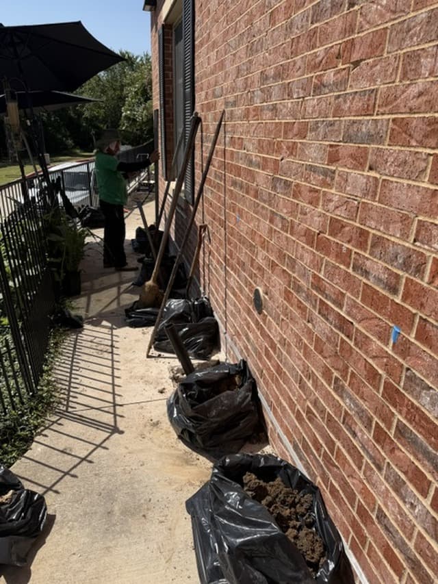 Hand-dug pier holes along a brick foundation with the soil bagged for cleanup
